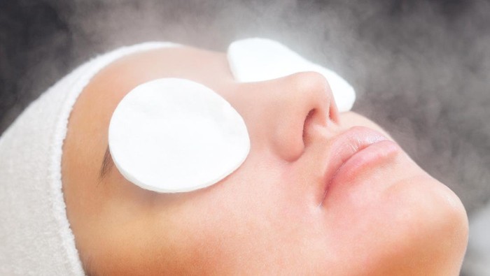 The procedure of steaming the skin of the face of a young woman before cleaning the skin in a cosmetology salon.