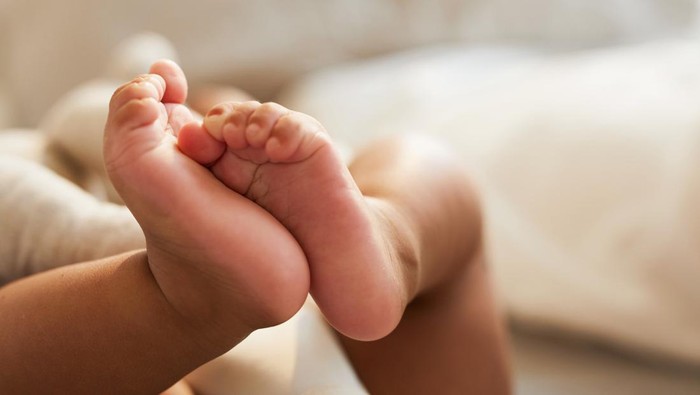 Close-up of unrecognizable cute baby shaking feet while lying in bed, innocence concept