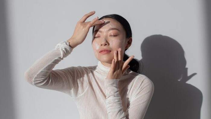 Foto perempuan menggunakan krim di wajah.