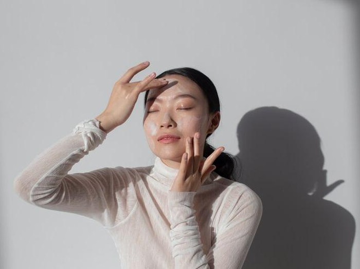 Foto perempuan menggunakan krim di wajah.