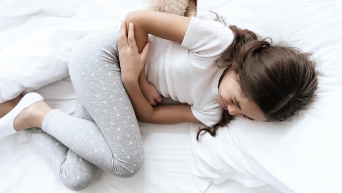The girl has a stomach ache. She feels bad and uncomfortable, then that it hurts. She holds her hands in her sore spot.