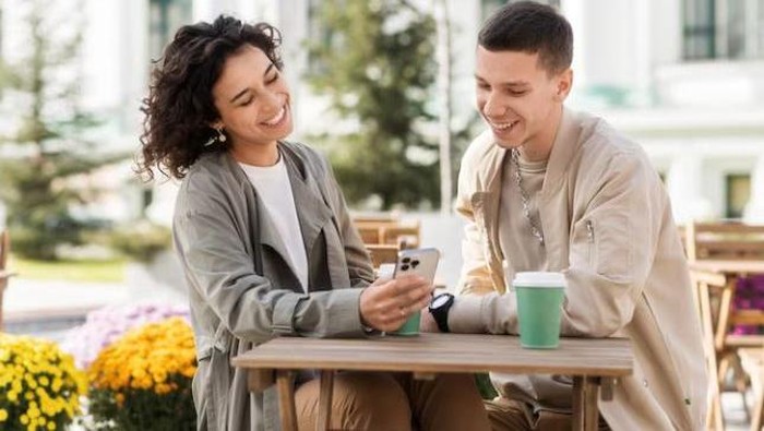 Perempuan dan laki-laki mengobrol sambil melihat handphone bersama