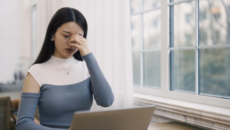 A young Asian woman, about 25 to 29 years old. She is wearing a grey dress, sitting in a cafe and working on a laptop. She was a little tired and stopped working to relax her body.