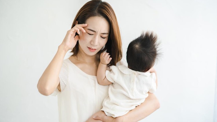 Asian mother holding a baby and looking tired