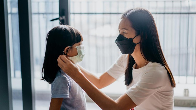 Image of an Asian mother helping her daughter wear a protective face mask to prevent virus infection