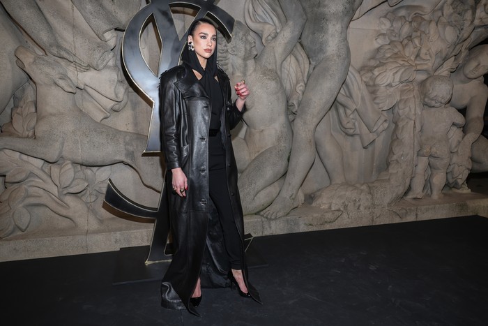 Masih dari YSL, Dua Lipa menampilkan gaya edgy ala era 80an lewat kombinasi mantel hitam dan jumpsuit aksen hoodie.Foto: Pascal Le Segretain/Getty Images