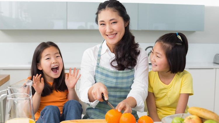 Portrait of a smiling woman with cheerful two daughters cutting fruit in the kitchen at home