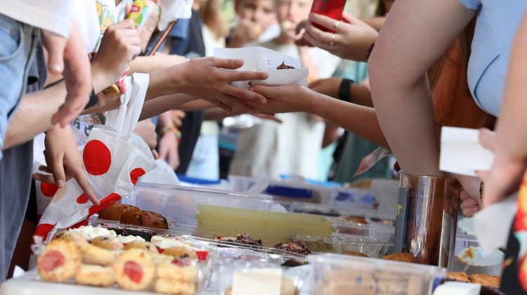 A close up of hands and food exchanging at a communty fair, fete or market stall. A typical bake or cake sale.