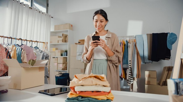 1387016543 Young Asian business owner woman use smartphone check order purchase online in home.