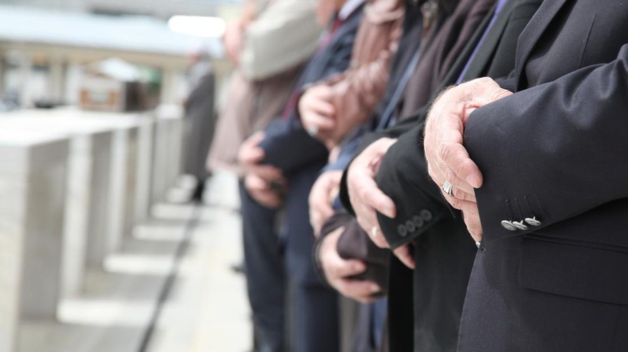Close Up Shot of Muslim People Tied Hands. One Person's Hand on Foreground is in Focus and the Others on Background is Out of Focus. Coffins also in front of the People. Islamic Ceremony for Dead People. Whorshippers Standing next to the Coffins and Pray.