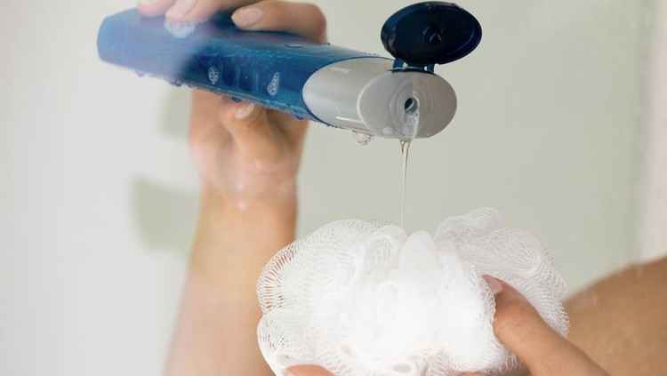 Close up young woman pouring liquid moisturizing soap shower gel from cosmetic bottle on loofah puff, enjoying morning evening body cleansing routine, removing dead cells exfoliating in bathroom.