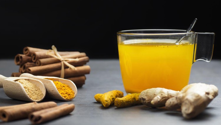 Herbal ginger and turmeric tea in glass cup with ginger root, dry turmeric, cinnamon sticks and their powder. Herbal spice tea for flu cold winter days