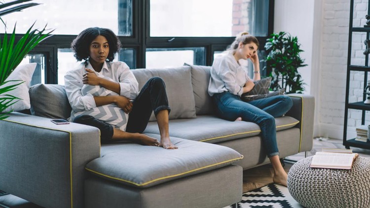 Portrait of offended dark skinned hipster girl sitting on cozy couch with disappointed fellow, unhappy multicultural friends don't talk after quarrel in modern apartment feeling stress from problems
