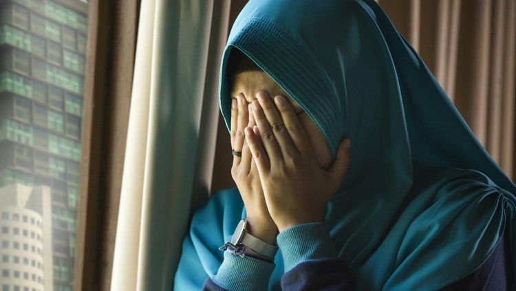 lifestyle portrait of young sad and depressed Muslim woman in Islam traditional Hijab head scarf at home window feeling unwell suffering depression crisis and anxiety problem crying helpless