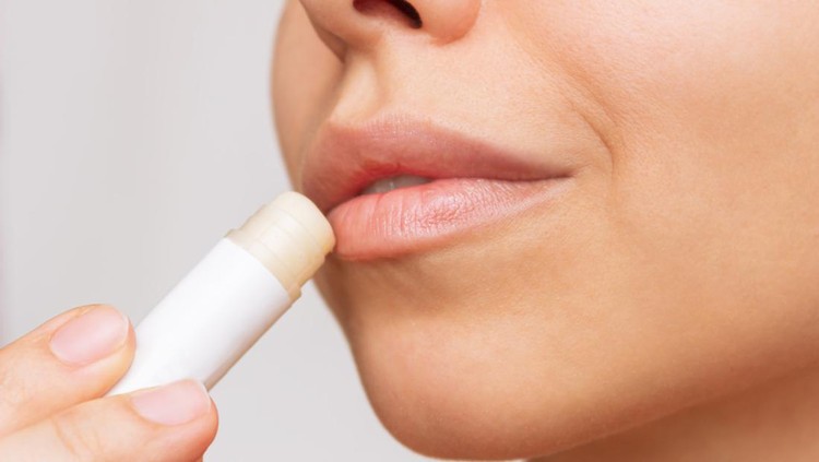 1353625145 Cropped shot of a young caucasian beautiful woman applying a hygienic lipstick on her lips on a gray background. Moisturizing chapstick for dry lips