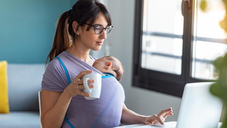 1213213366 Shot of pretty young mother with her baby in sling drinking coffee while working with laptop at home.