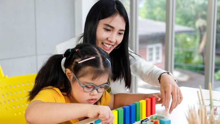 Asian girl with Down's syndrome play puzzle toy with her teacher in classroom.