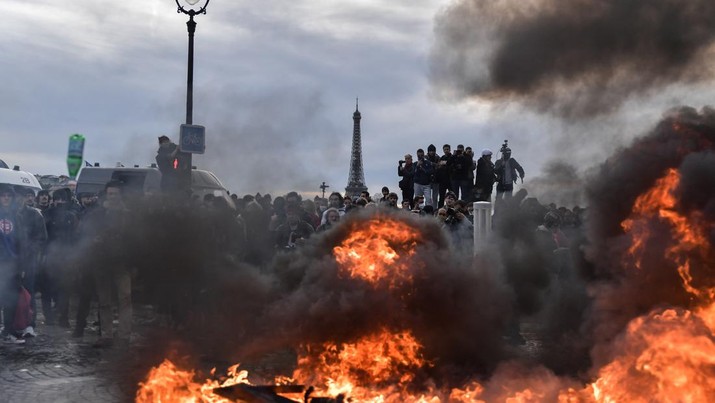 Menara Eiffel terlihat saat pengunjuk rasa membakar saat bentrokan terjadi dengan polisi anti huru hara selama demonstrasi menentang rencana pemerintah Prancis untuk menaikkan usia pensiun resmi di Paris, pada 16 Maret 2023. (Firas Abdullah/Anadolu Agency via Getty Images)