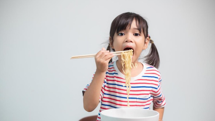 Cute Asian child girl eating delicious instant noodles at home.