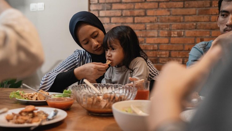 Ilustrasi Manfaat Puasa Bagi Kesehatan Anak muslim mother feeding her toddler child during dinner with family