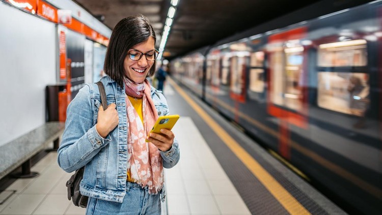 Beautiful young woman using smart phone in a subway station while waiting for her subway.