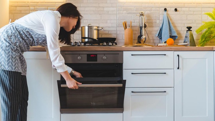 1150675702 young pretty woman open oven to cook. domestic kitchen concept. copy space