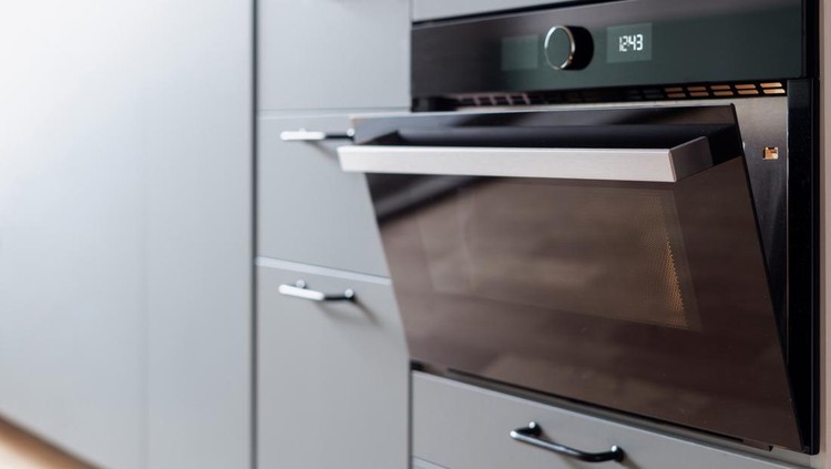 closeup of electric built in oven with opened door and light inside and modern cupboard at apartment kitchen