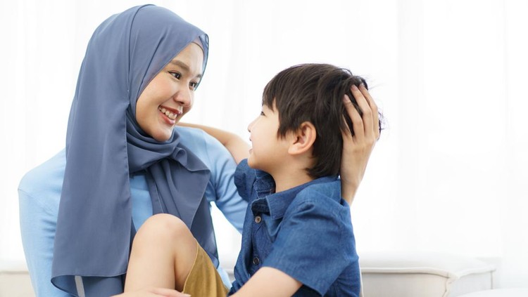 Happy cheerful Asian muslim family stay together in living room in weekend, Beautiful Asian woman muslim and lovely little boy portrait and looking at camera.