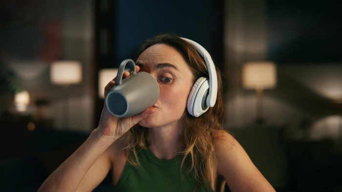 Pleased woman listening headphones at dark place. Positive freelancer dancing rejoicing music at modern flat closeup. Successful girl drinking coffee at night apartments. People emotions concept