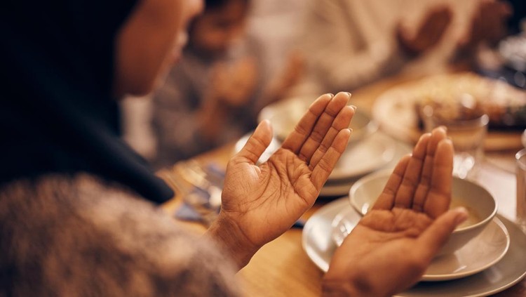Close-up of religious Muslim woman and her family praying before the meal at dining table on Ramadan.