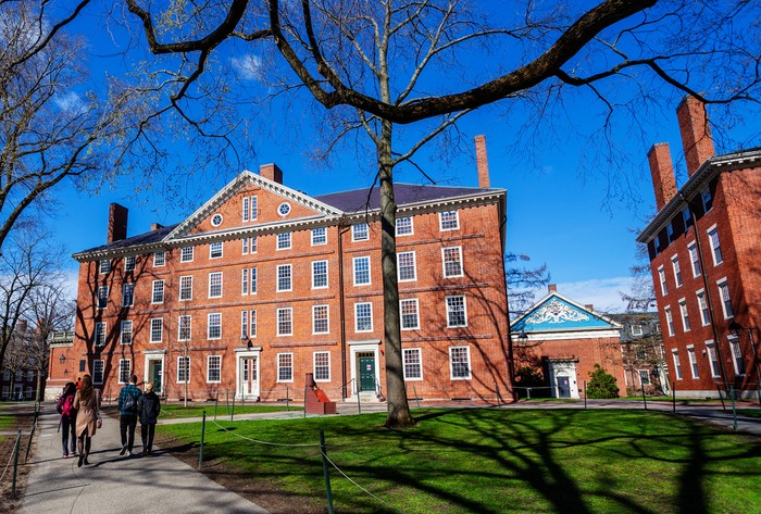 Cambridge, Massachusetts, USA - April 10, 2022: Students walking in Harvard Yard towards freshman dormitory building Hollis Hall . Built in 1763, it is one of the oldest buildings at Harvard College.