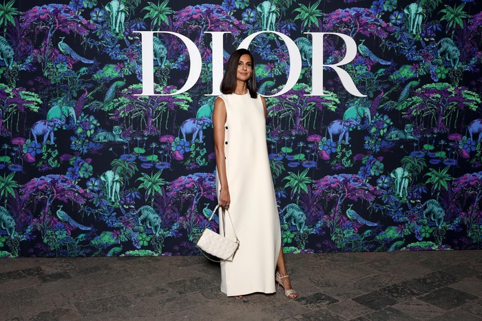 Poorna Jagannathan tampil minimalis dan chic memakai gaun putih aksen slit dan tas senada. Foto:Getty Images/Courtesy of Dior