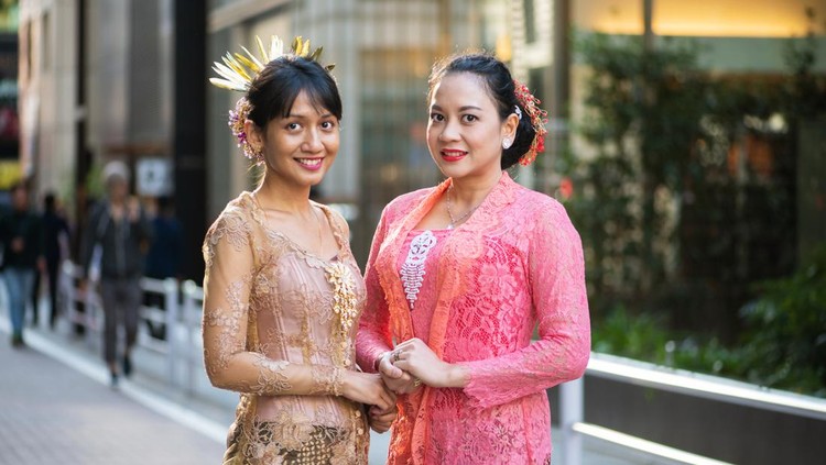 1143196447 Two mid adult women in traditional Indonesian clothes, smiling for the camera while standing outside.