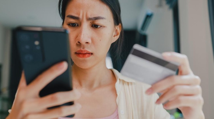 Close-up Youth asia female wear casual sit front of desk hold smartphone and credit card feel upset online shopping payment declined credit over limit in living room at house. Home lifestyle concept.