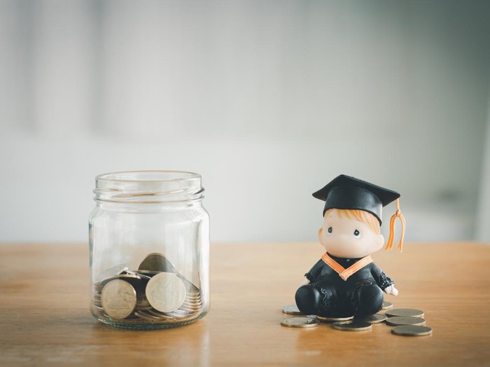 Education savings concept. Coins in a glass jar for education money savings with a graduate doll. Personal financial planning for the future.
