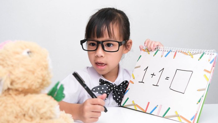 Cute Asian little girl playing teacher role game. A little girl is teaching math to her teddy bear friend. Homeschool children's play and learning.