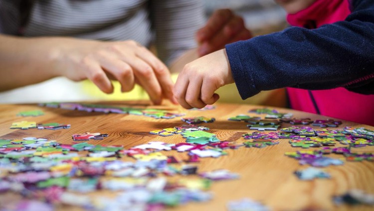 Hands of a little child and parent plying jigsaw puzzle game on a wooden table