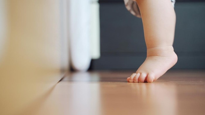 Little toddler learning to stand on the wooden floor, Baby feet.