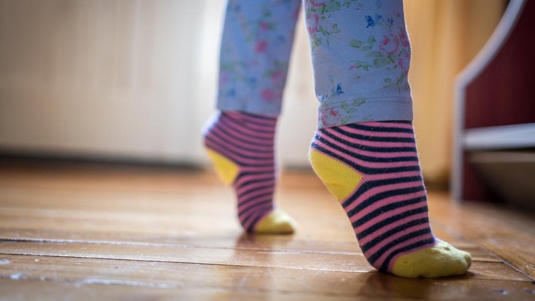 Little toddler learning to stand on the wooden floor, Baby feet.
