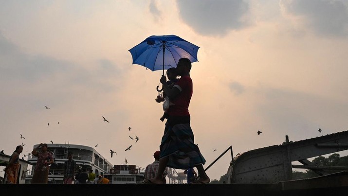 A man carrying his son walks with an umbrella during a heatwave in Yangon on April 19, 2023. (Photo by Sai Aung MAIN / AFP) (Photo by SAI AUNG MAIN/AFP via Getty Images)