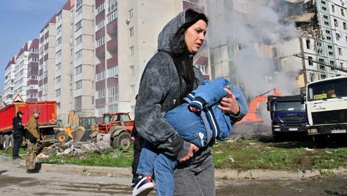 A woman walks past damaged residential buildings as she carries a child in Uman, around 215km southern Kyiv, on April 28, 2023, after Russian missile strikes targeted several Ukrainian cities overnight. - Ukraine and Russia have been fighting since Moscow's February 2022 invasion and Ukraine says it has been preparing for months a counter-offensive aimed at repelling Russian forces from the territory they currently hold in the east and south. (Photo by Sergei SUPINSKY / AFP) / The erroneous mention[s] appearing in the metadata of this photo by Sergei SUPINSKY has been modified in AFP systems in the following manner: [in Uman, around 215km southern Kyiv,] instead of [in Kyiv]. Please immediately remove the erroneous mention[s] from all your online services and delete it (them) from your servers. If you have been authorized by AFP to distribute it (them) to third parties, please ensure that the same actions are carried out by them. Failure to promptly comply with these instructions will entail liability on your part for any continued or post notification usage. Therefore we thank you very much for all your attention and prompt action. We are sorry for the inconvenience this notification may cause and remain at your disposal for any further information you may require.