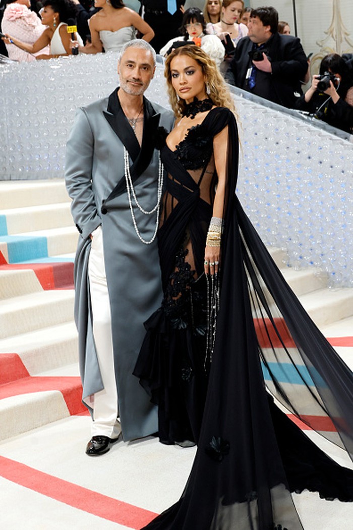 Rita Ora dan Taika Waititi bergaya eklektik dan seksi dalam gaun hitam yang dramatis dan mantel panjang klasik serta sematan aksesori. Foto: Getty Images/Mike Coppola