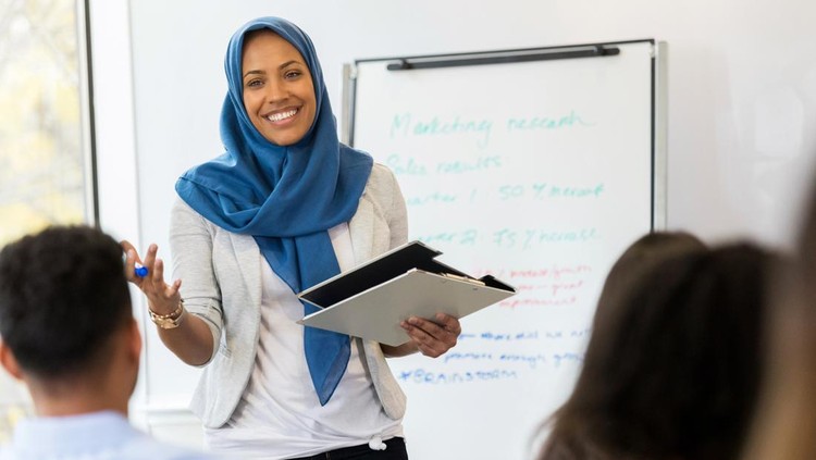 1132123970 A mid adult Muslim businesswoman smiles as she speaks to a group of employees during a training class.