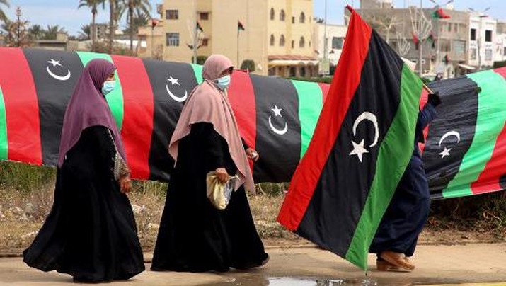 A Libyan woman carries a national flag in the capital Tripoli on February 25, 2021, during celebrations commemorating the 10th anniversary of the 2011 revolution that toppled longtime dictator Moamer Kadhafi. - Libya's prime minister-designate Abdul Hamid Dheibah is set to name a transitional government tasked with unifying the war-torn nation and leading it to elections in December. (Photo by Mahmud TURKIA / AFP)