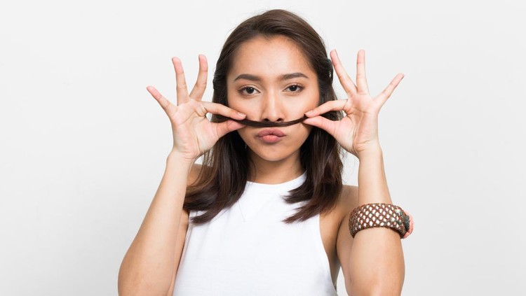 Studio shot of beautiful Asian woman making mustache using her hair
