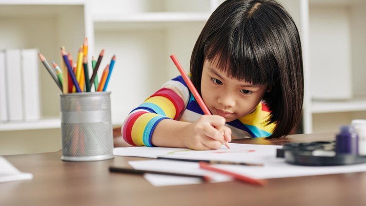 1219837048 Adorable talented Asian girl sitting at desk at home and drawing with red pencil