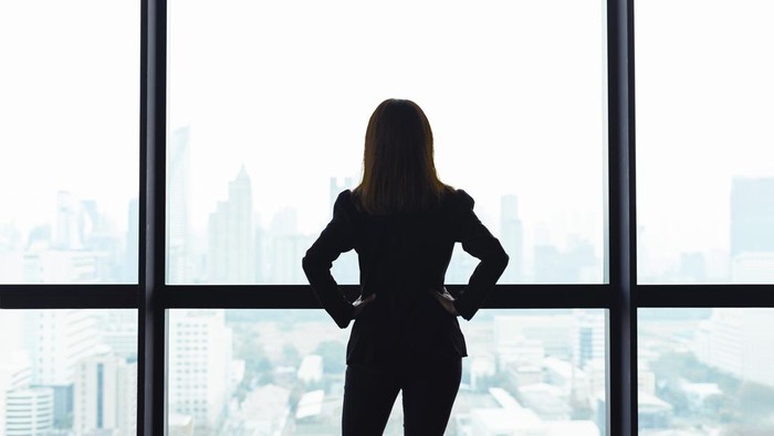 Asian business woman with arms akimbo looking out the window at city view background