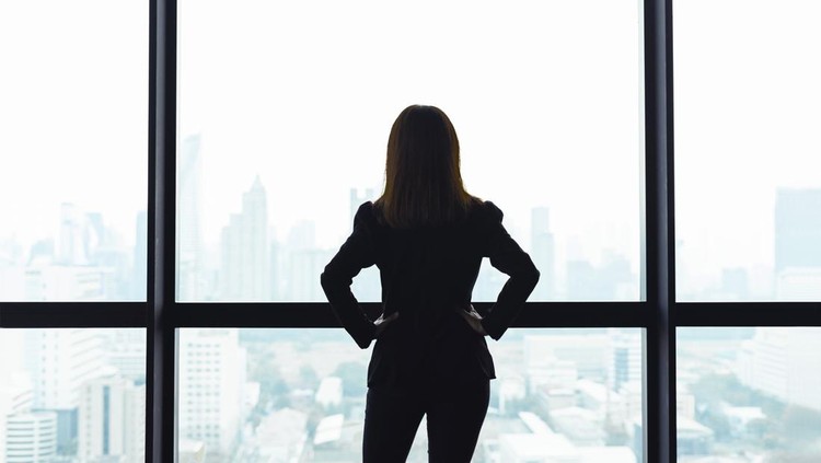 1139808595 Asian business woman with arms akimbo looking out the window at city view background