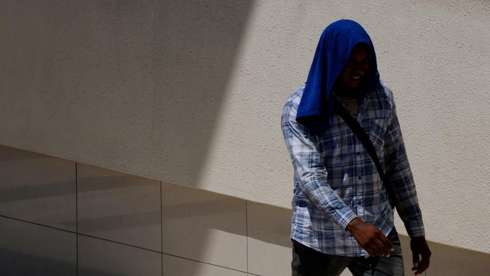 Seorang pekerja migran melindungi kepalanya dari sinar matahari dengan handuk di hari yang hangat di Singapura, 15 Mei 2023. (REUTERS/Edgar Su)