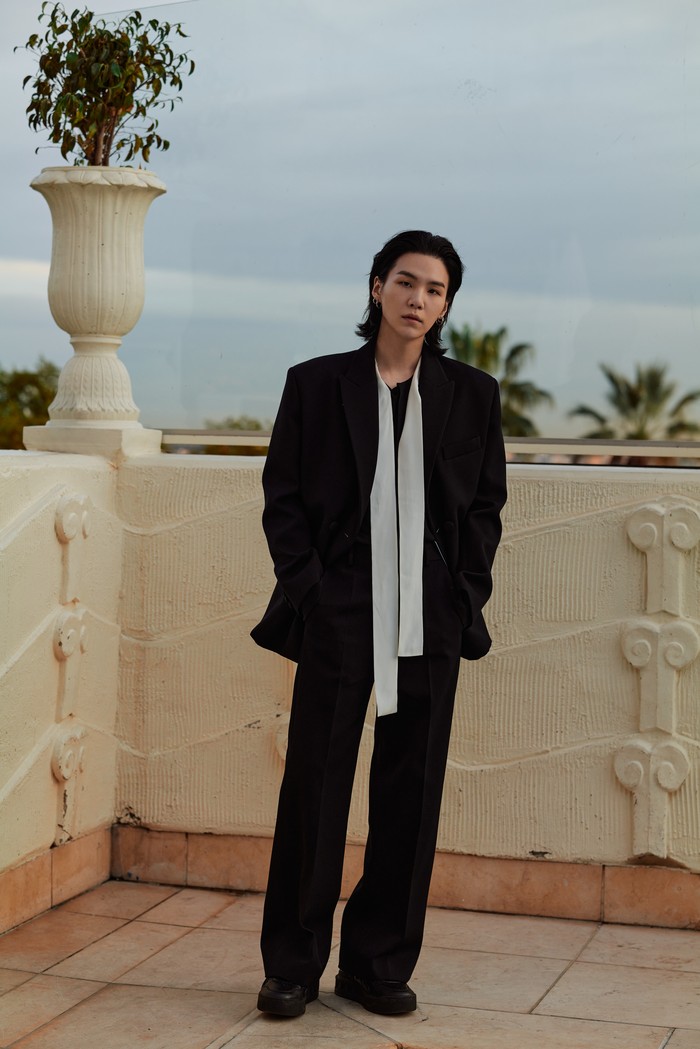 Suga terlihat stylish dalam padanan setelan dan blus aksen pita. Gayanya juga membuktikan bahwa pantsuit tak harus selalu dipasangkan dengan kemeja. Foto: Courtesy of Valentino